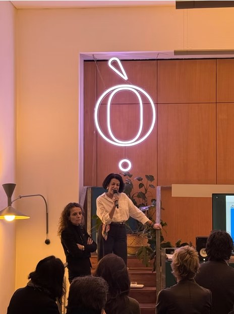 La serata Ottanio OpenDoor sotto l’insegna al neon Ò, con la relatrice al microfono